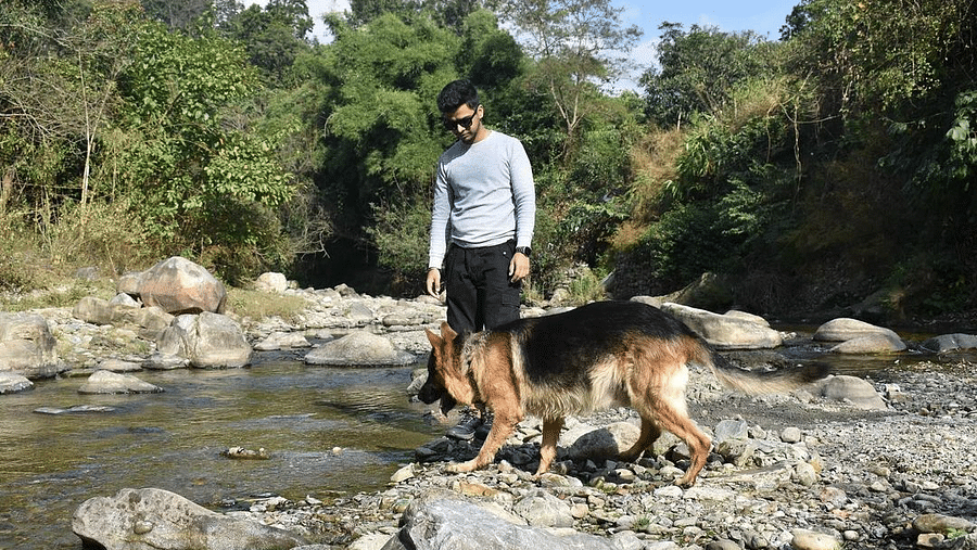 A man with a dog standing on the edge of a stream at the Sylvan Retreat, Dehradun.