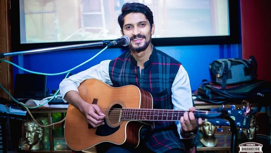 An image of a man playing guitar and singing on a mic at the same time at Themis Barbecue House, NSP Panipat
