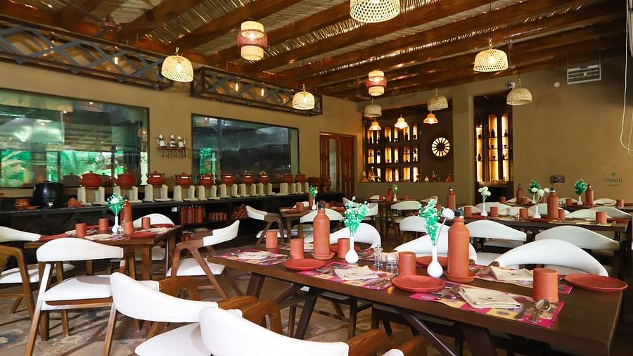 a cosy restaurant decked with plush seating arrangements and large windows at Themis Mudhouse - A Nature's Retreat Resort & Wellness