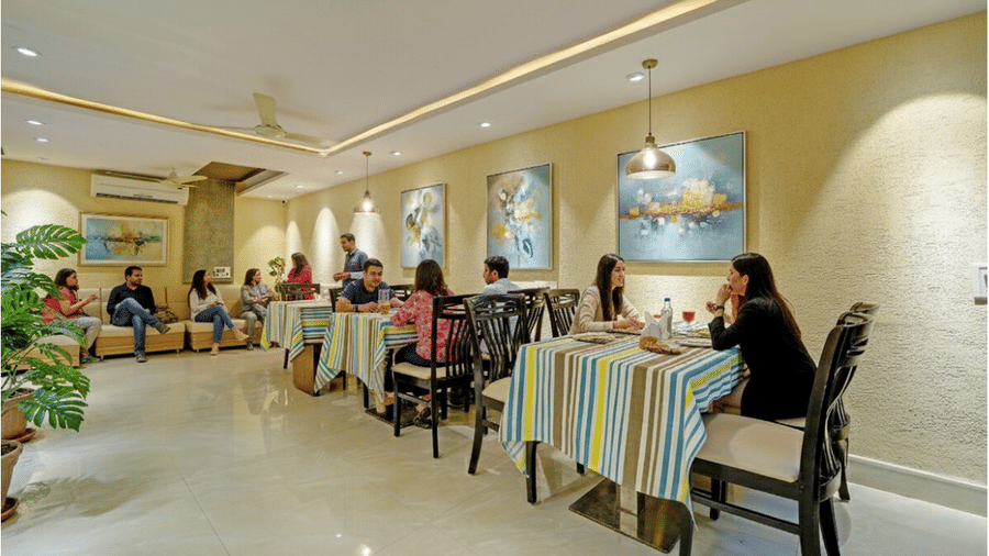 Guests dining at striped tablecloth tables in a well-lit restaurant with wall art at Maurya Hotel, Bhopal..