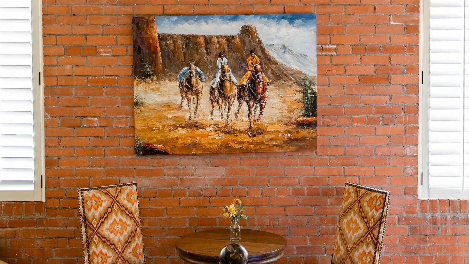 A room with a rustic brick wall, a beautiful painting of horses, and stylish seating, creating a warm, artistic atmosphere - The Grand Hotel & Ballroom, McKinney