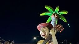 The night view of the a boy big statue playing guitar surrounded by big palm tree and lights