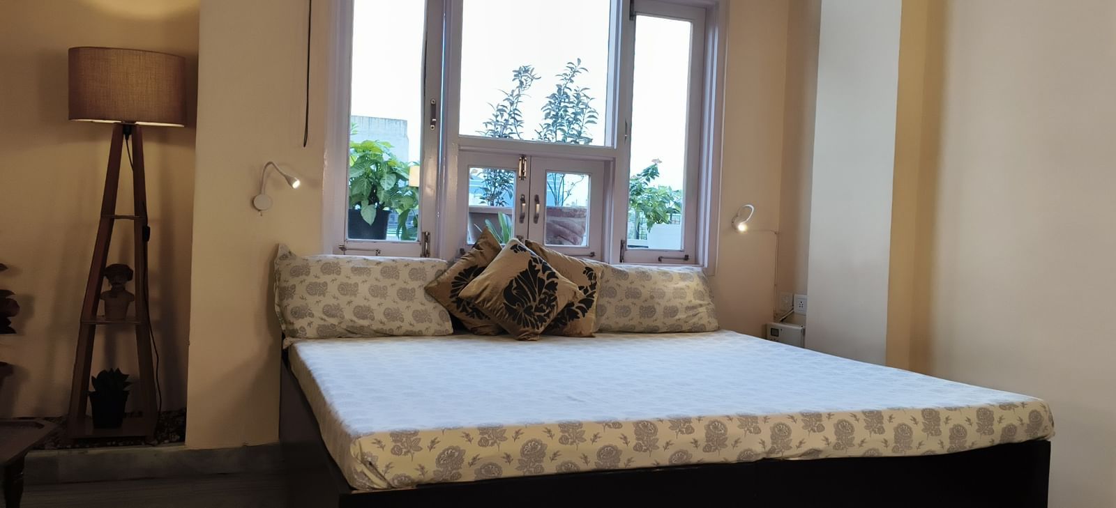 A room with a double bed placed by the windows and a standing lamp nearby at Jaypore360 Homestay in Jaipur.