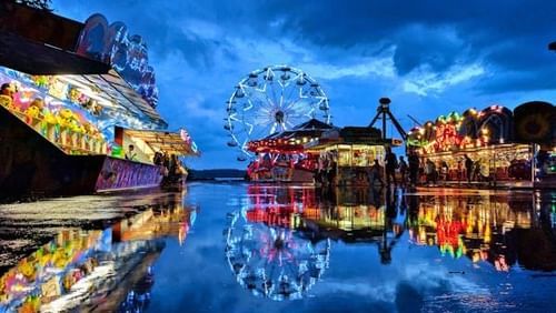 A colourful image of a carnival setup with giant wheel and shops.