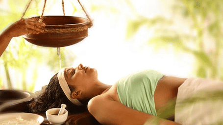 Woman receiving an Ayurvedic therapy with oil being gently poured on her forehead at a spa.