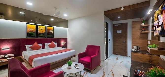 A room featuring a neatly made bed, a seating area, and a dressing table at Angel Lords Eco Inn Amreli.
