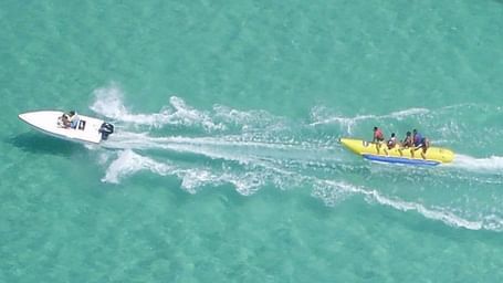 Excited riders on a banana boat whipped by a speedboat.