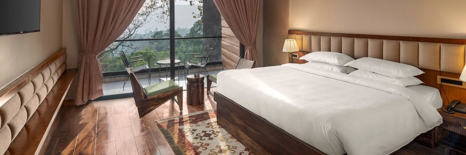 A cosy bedroom with a wooden floor and ceiling, large draped window with a scenic view, and a comfortable sitting area - The Samai, Bhimtal