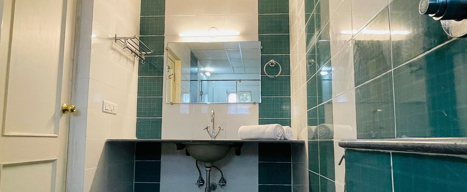 A bathroom featuring teal and white tiling and a sleek washbasin with a mirror at Sanctum Suites Indiranagar, Bangalore.