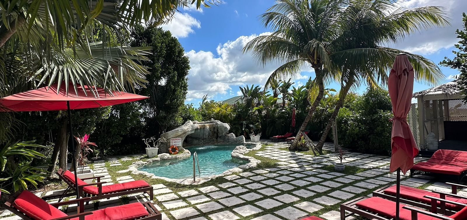 Poolside seating with red lounge chairs and umbrellas surrounded by palm trees | A Stone's Throw Away