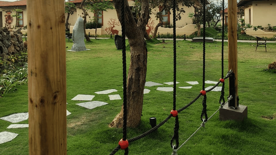 An outdoor play area featuring suspended ropes with black footholds attached to tall wooden posts at Hotel Sonar Bangla, Ajodhya Hills.