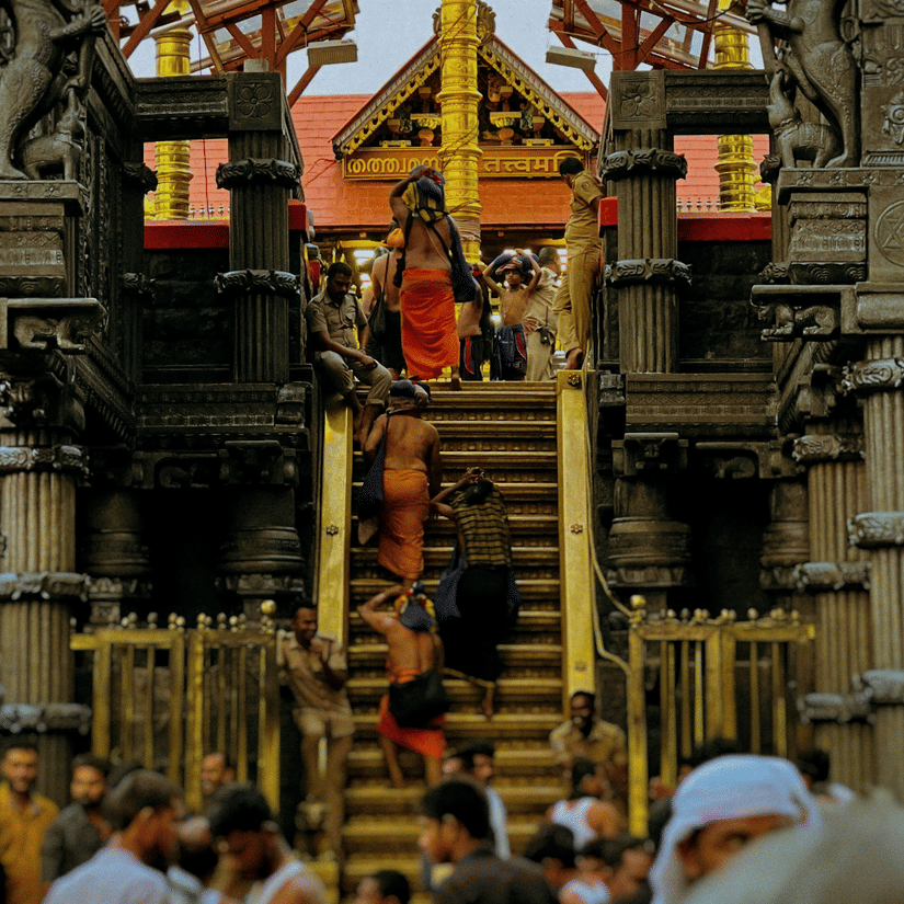 A view from below of numerous people near a temple and some walking along the steps towards the temple. The Sita Gufa history is infamous for it's mention in the Ramayana.
