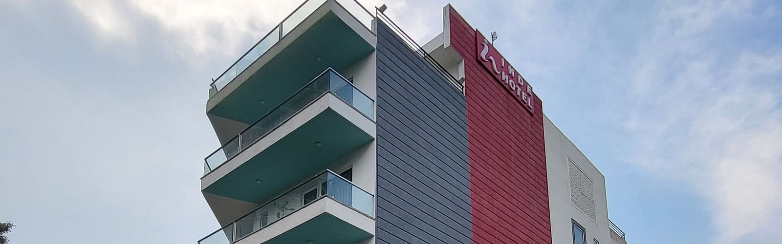 A facade of Inde Hotel Golf Course Extension featuring multiple storeys and balconies on each floor, and cars parked on the lawn