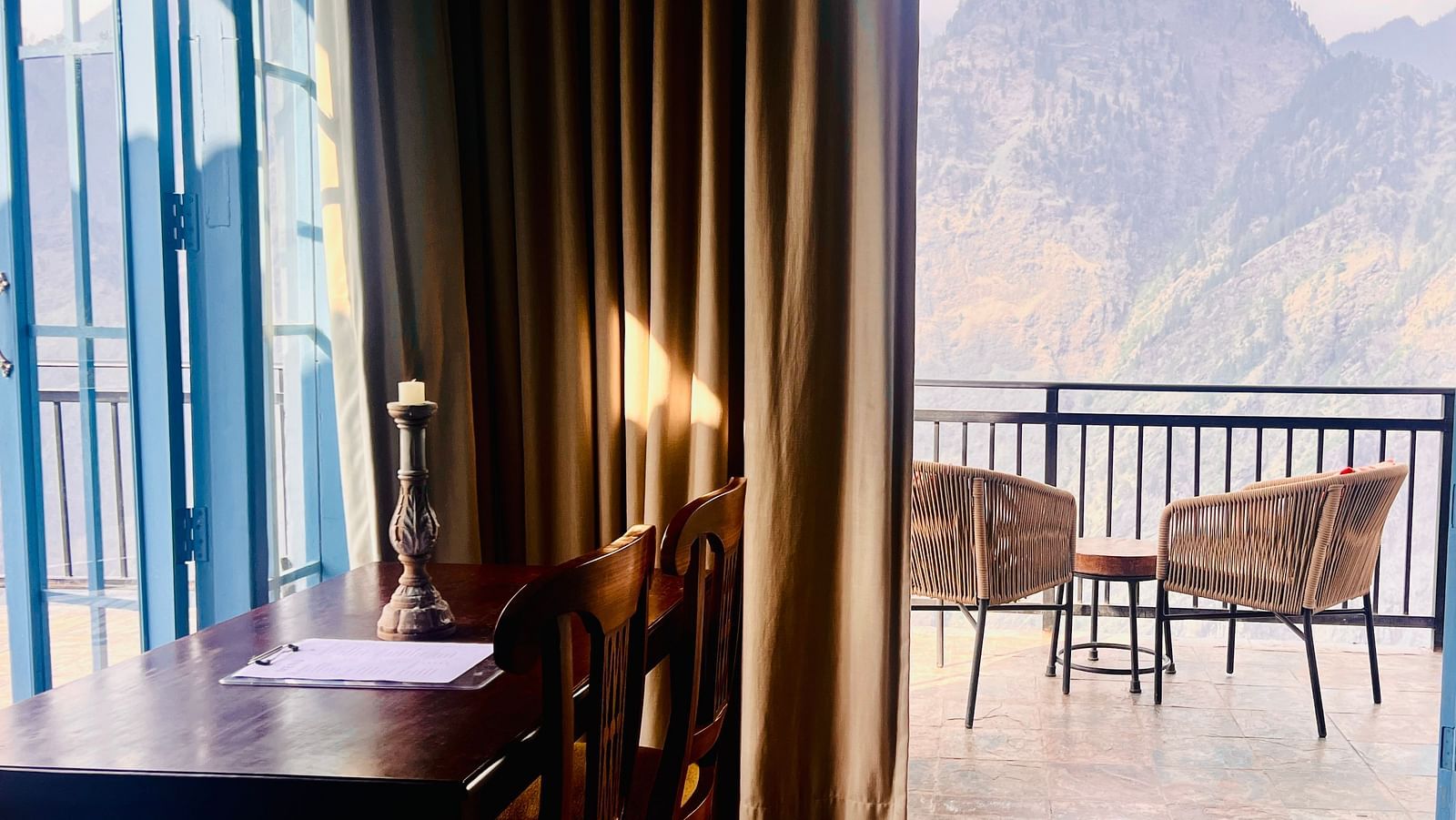 Cozy dining area with a wooden table and chairs overlooking a mountain view through large glass windows in a luxury hotel | Faraway Cottages, Auli