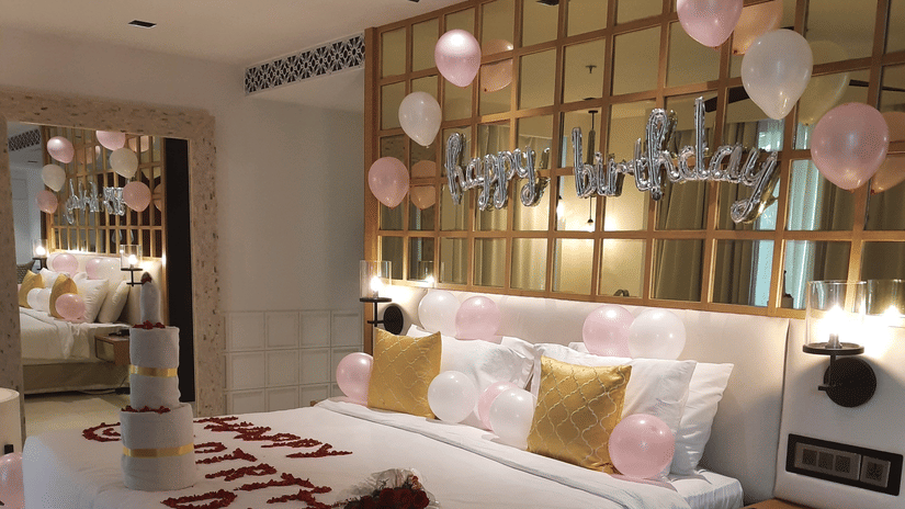 A hotel room decorated with balloons and rose petals on the bed for a romantic occasion.