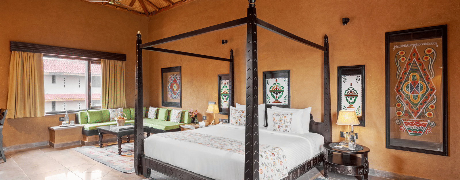 An interior shot of a room featuring a traditional four-poster bed and decor, with a high ceiling and windows at Aamaghati Wildlife Resort.