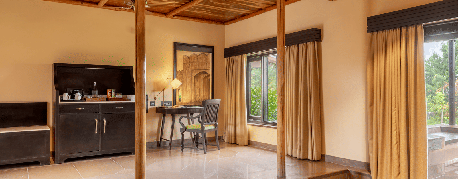 The spacious interior of a room with a seating area, high ceilings with exposed beams, and a view of the outside at Aamaghati Wildlife Resort.