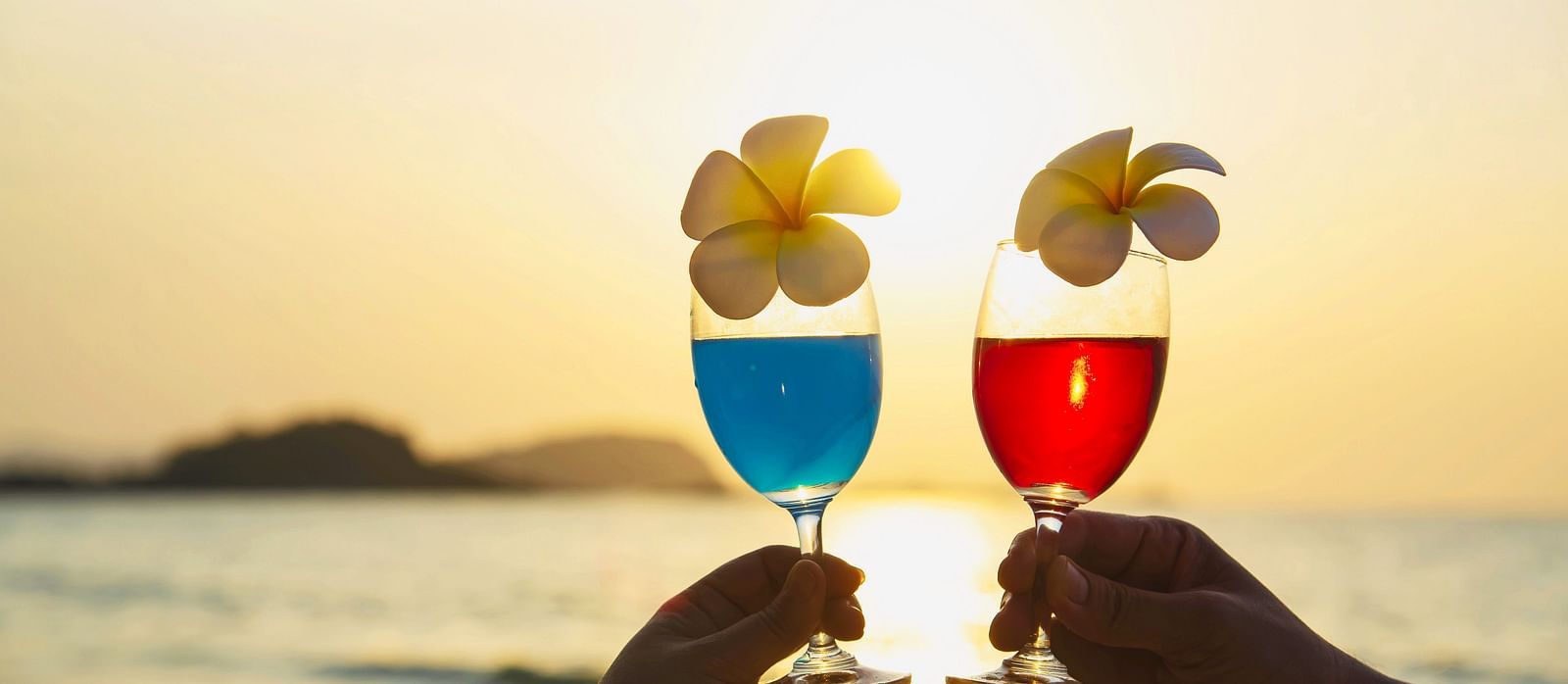 Two people toasting with colourful cocktails adorned with flowers at sunset - Alibu Resort Nha Trang