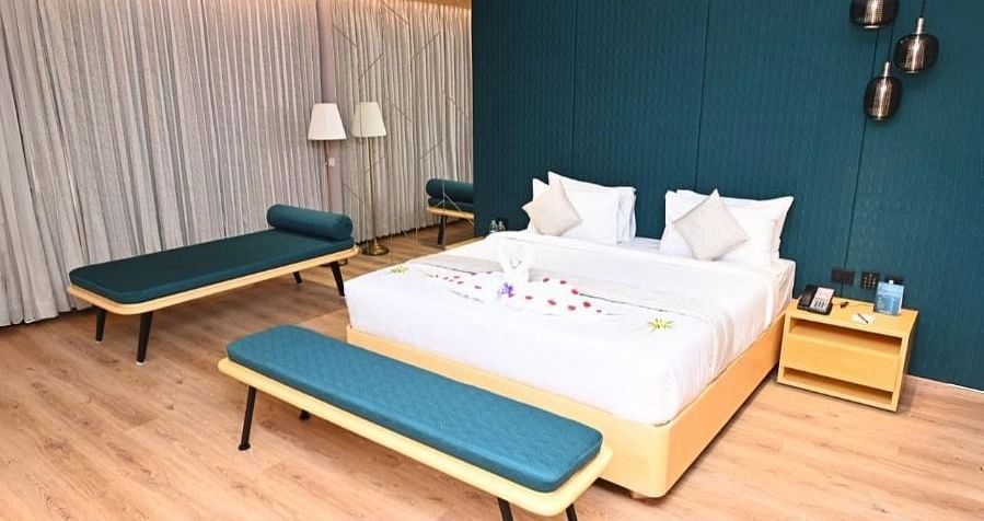 A bedroom in Dhanalakshmi Srinivasan Hotels, Perambalur, with a large bed, two lounge chairs, and two armchairs. The room features wooden flooring and a dark blue accent wall.