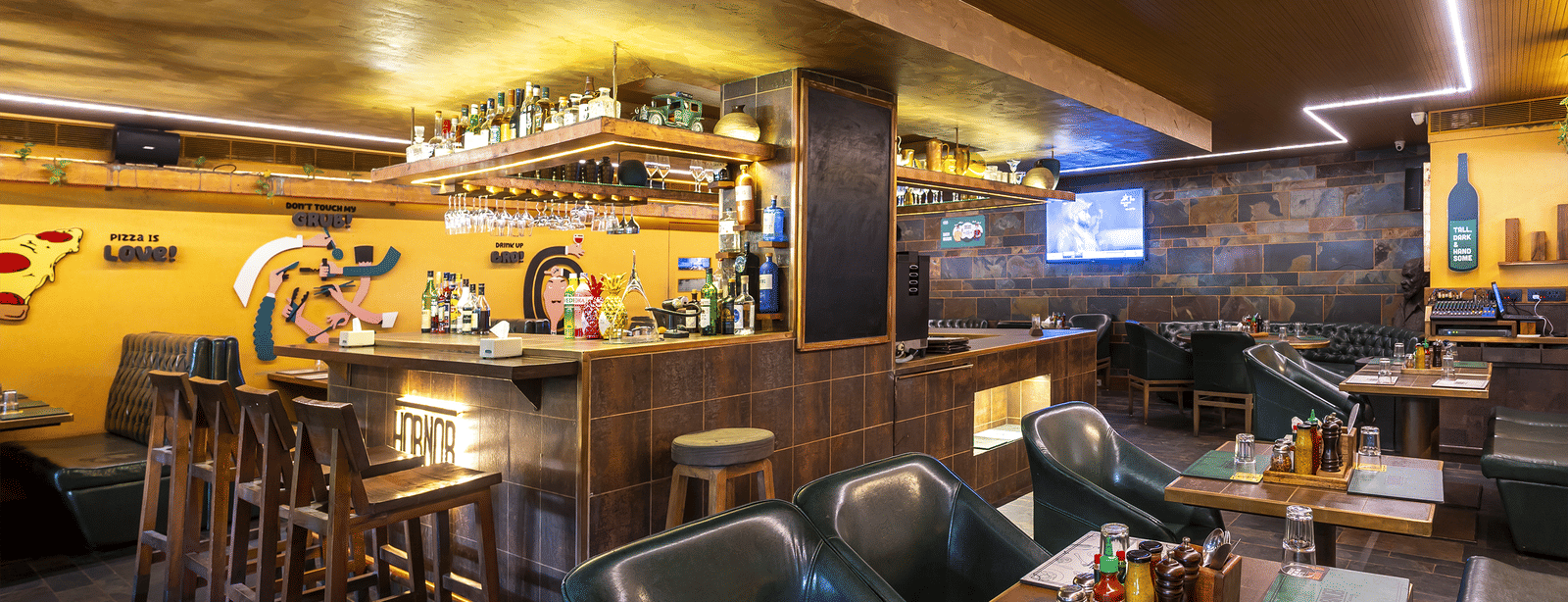 A restaurant interior with high tables, chairs and wall murals in a rustic wooden setting at Infiniti Hotel, Indore.