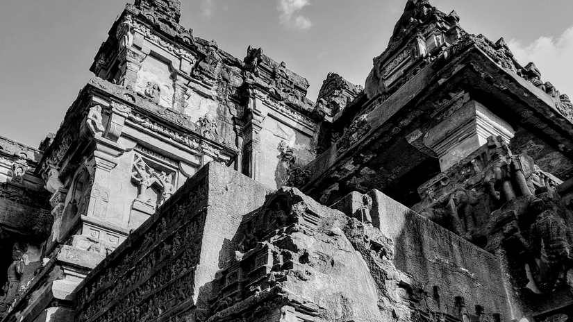  a massive ancient Indian rock-cut monolithic structure with intricate carvings, under a cloudy sky