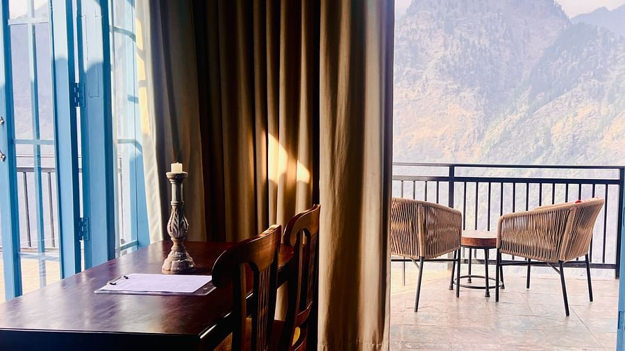 Cozy dining area with a wooden table and chairs overlooking a mountain view through large glass windows in a luxury hotel | Faraway Cottages, Auli