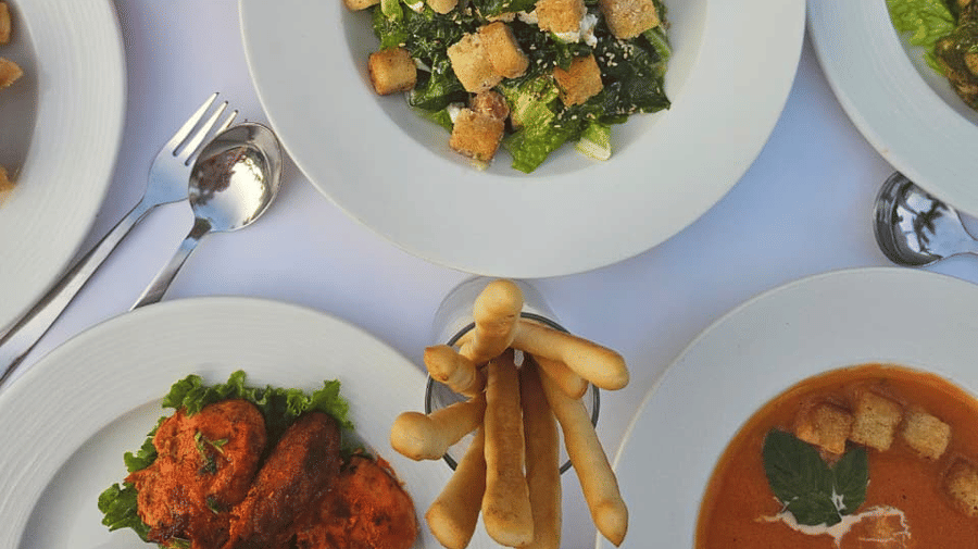 Multiple plates of neatly arranged food placed alongside cutlery and fresh juice on a clothed table at A.S. Hotels, Khajuraho.
