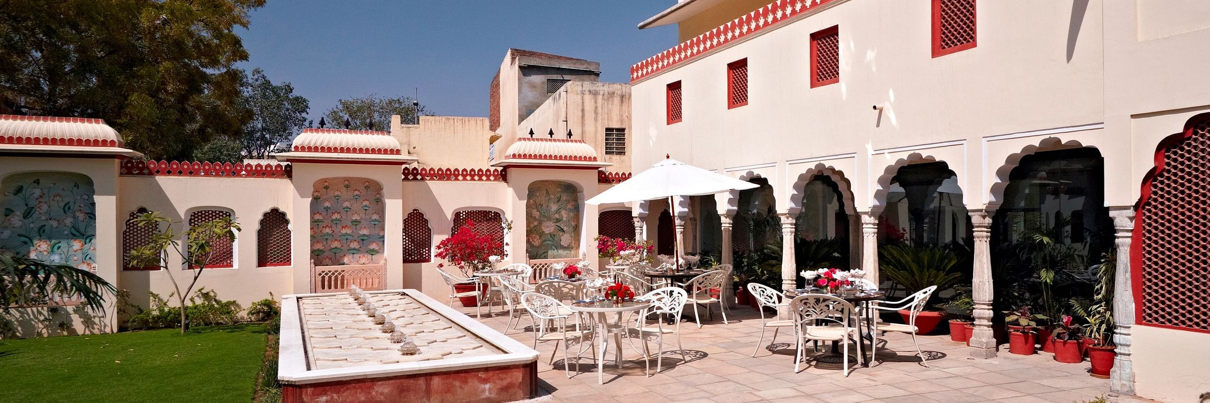 Seating arrangments in an open air setting with a fountain next to grass - Mandawa Haveli, Jaipur
