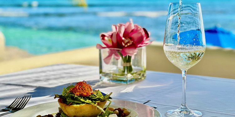 Close-up of an elegantly plated vegetarian meal with wine being poured into a glass on an outdoor table overlooking the ocean at The Soco Hotel.