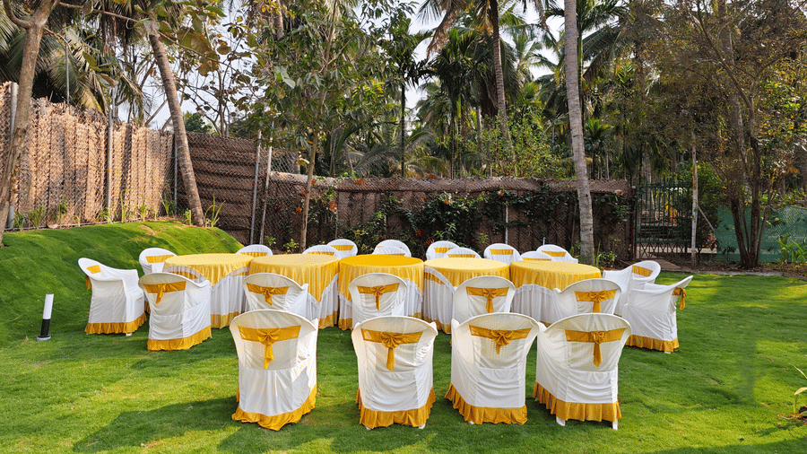 Tables and chairs arranged in the wedding lawn with trees in the backdrop at Ibex Resorts, Coimbatore (Kakarla).