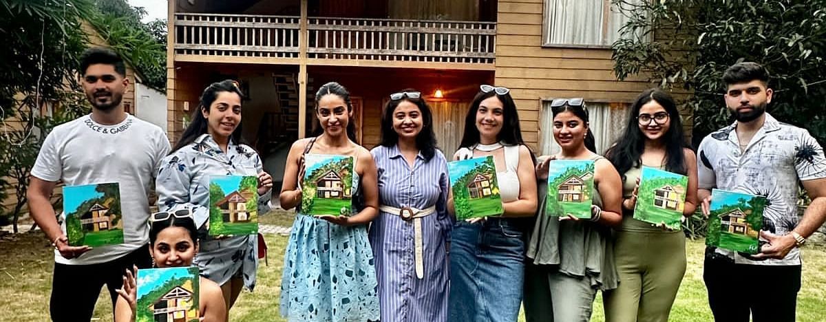 A group holding a canvas painting in front of Pinewood Cottage at the Sylvan Retreat, Dehradun.
