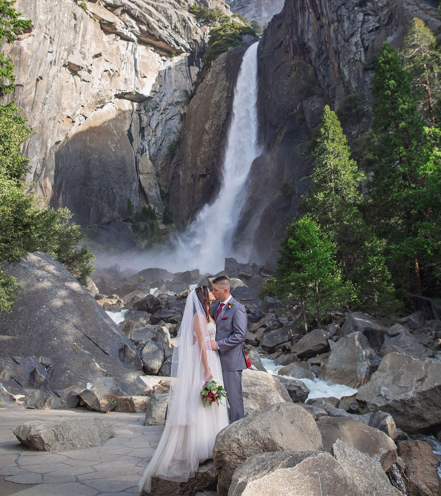 A couple posing for a wedding photoshoot in front of a waterfall in Yosemite - Narrow Gauge Inn - A Serenite Hotel Near Fish Camp.