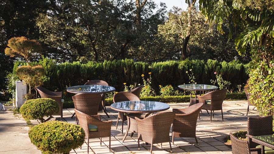 An outdoor seating area at The Claridges Nabha Residence in Mussoorie, featuring several tables and chairs, all arranged to overlook a forest view