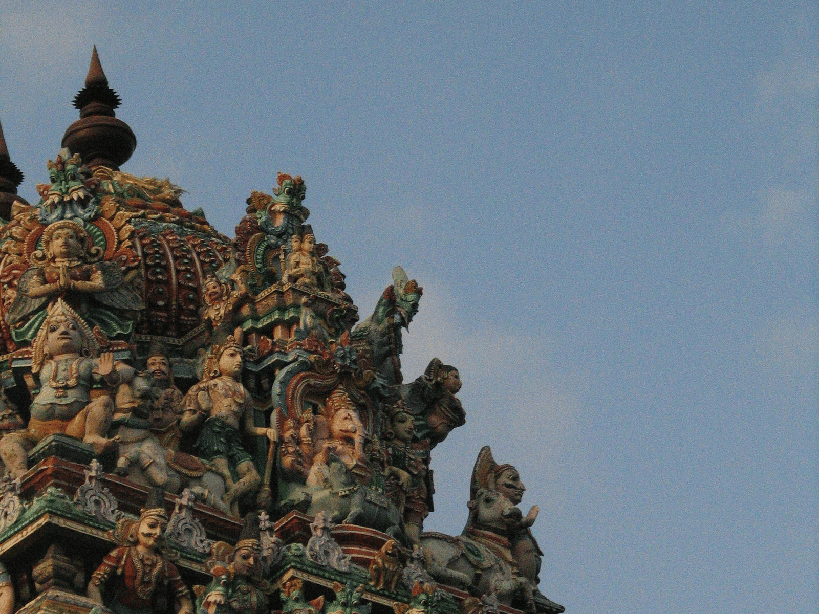 Close-up of detailed stone carvings on a temple gopuram with a cloudy sky backdrop.