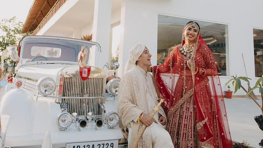 A bride and groom posing for a photo in front of a vintage car.