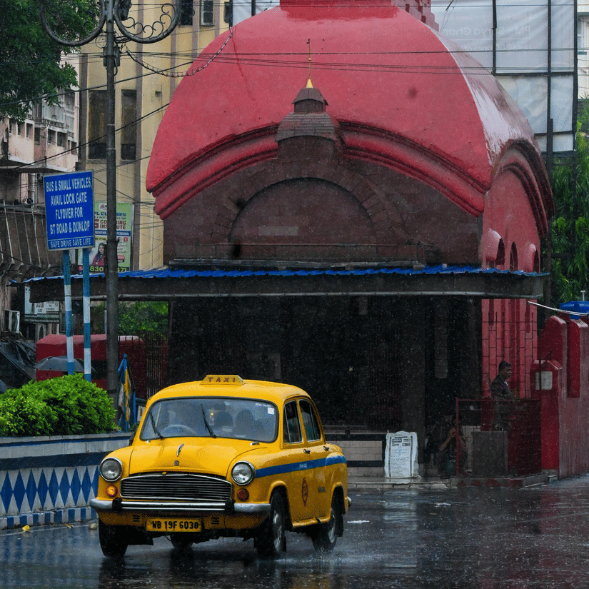 A yellow taxi passing by on a road in Kolkata during monsoon.