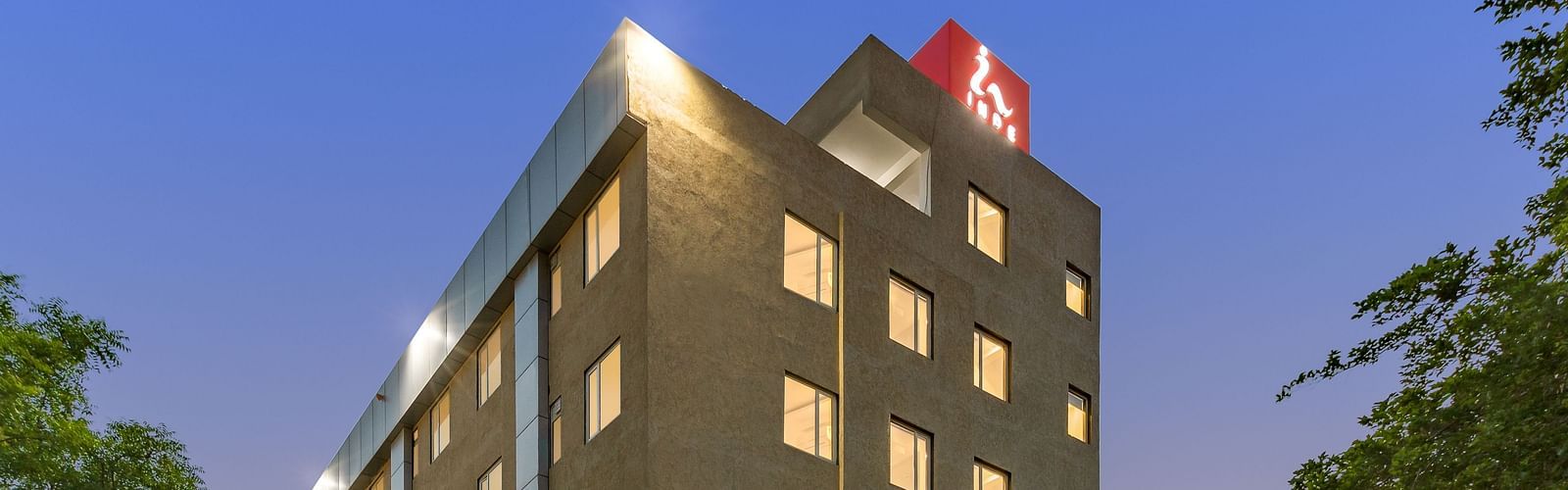 A facade image of a well-lit Inde Cyber City, Gurgaon building and beyond it an evening sky can be seen in the background - Inde Hotels & Resorts