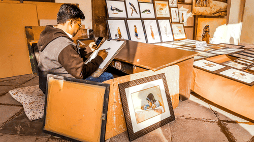 a person painting while sitting in a room filled with paintings