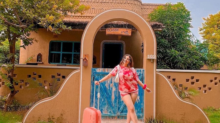 a woman standing in front of the gate with a luggage at Themis Mudhouse - A Nature's Retreat Resort & Wellness