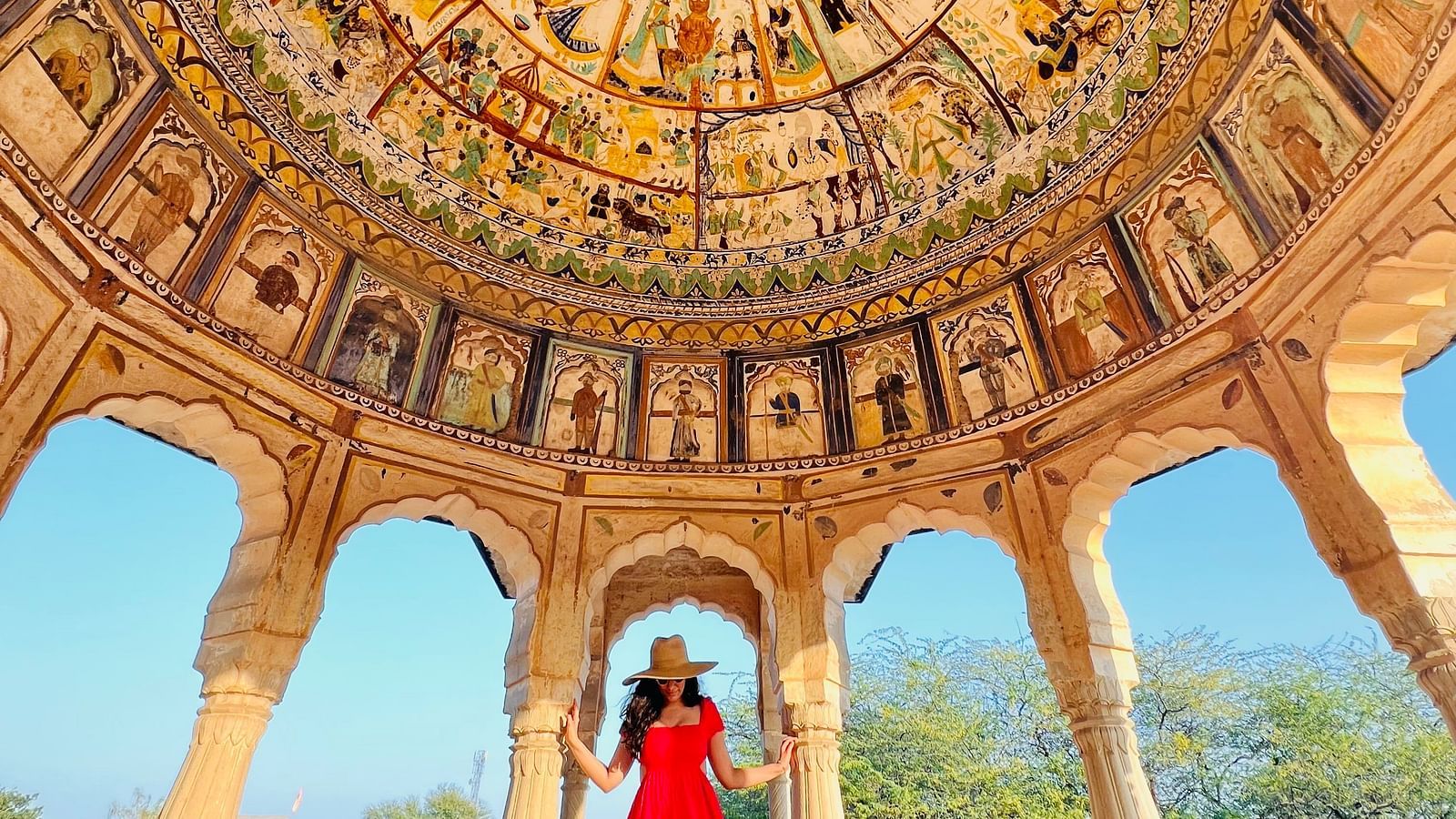 A person stands under a dome with detailed paintings and arched supports - Fort Barli, Ajmer.