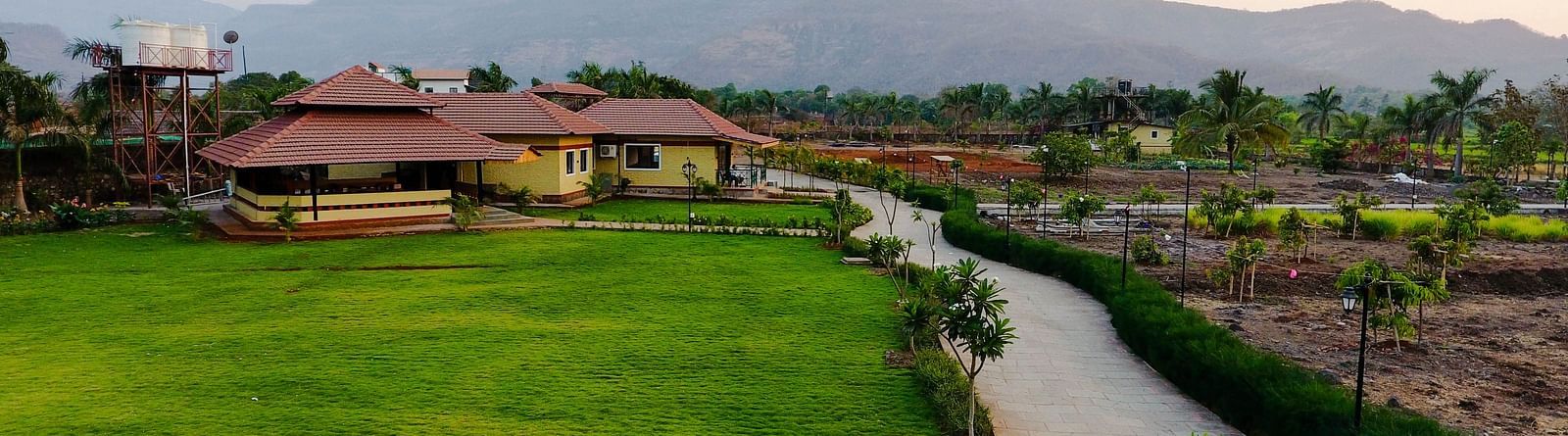 An aerial view of a pathway surrounded by lush green park, trees and houses in the distance | The Kanila Resort