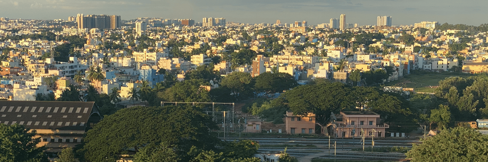 A wide aerial view of a dense urban city under a cloudy sky with a train track in the foreground.
