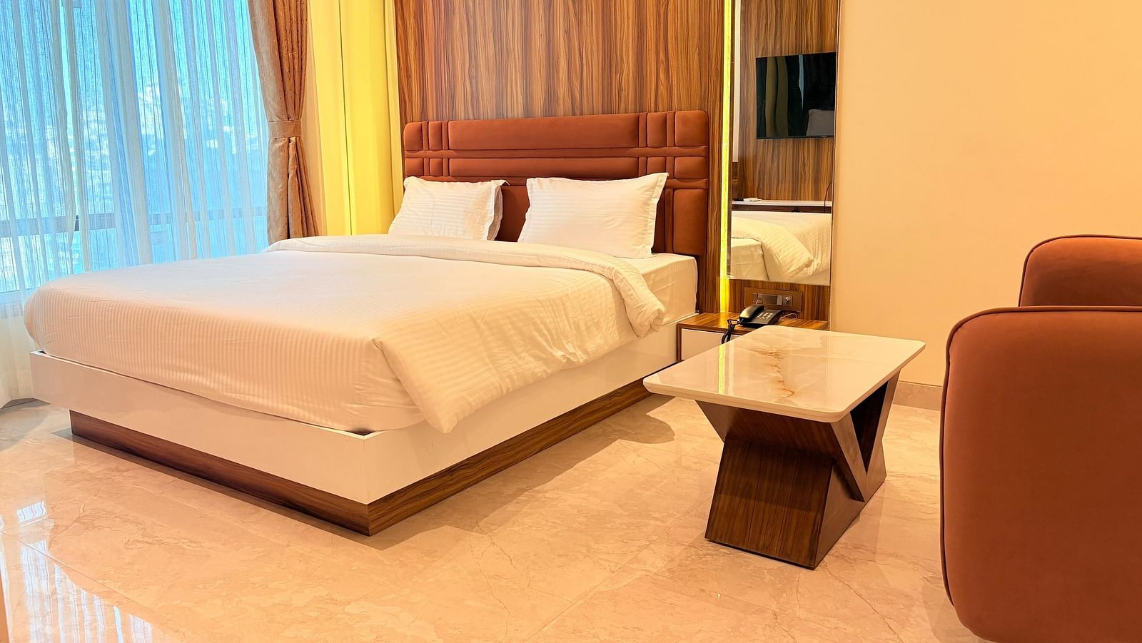 A bed with a wooden headboard and a television reflected in the mirror at Hotel Mumbai House, Vashi.