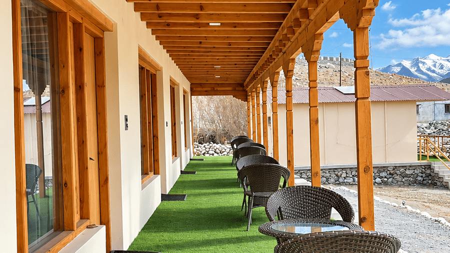 Covered outdoor walkway with wooden ceiling, property windows, chairs and green flooring.