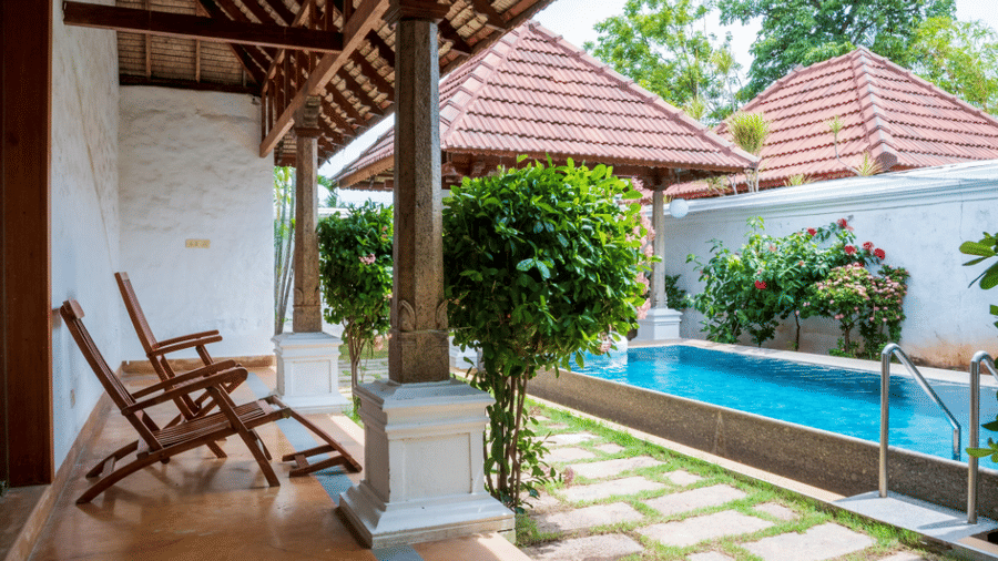 An outdoor private lap pool with 2 wooden lounge chairs under a covered patio next to a villa garden | Le Pondy