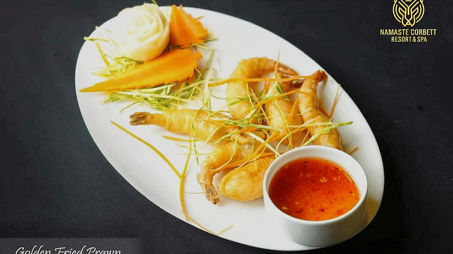 Golden fried prawns served with sweet chili sauce and vegetable garnish on a white plate.