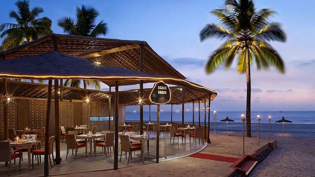An inviting beachside restaurant with open-air seating, illuminated warmly as the evening sets in, creating a perfect dining ambiance by the sea.