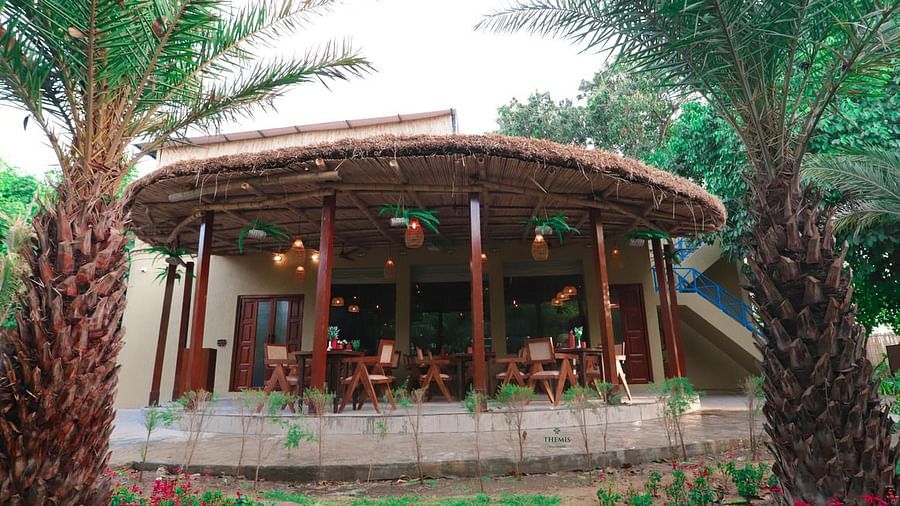 outdoor restaurant with a thatched roof at Themis Mudhouse - A Nature's Retreat Resort & Wellness
