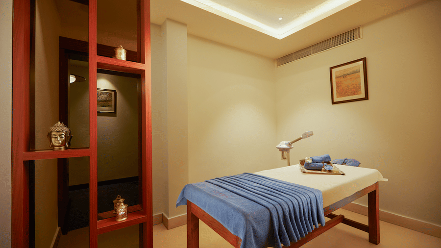 A massage table with a folded cloth in a room with a red-framed partition and a small picture on the wall.