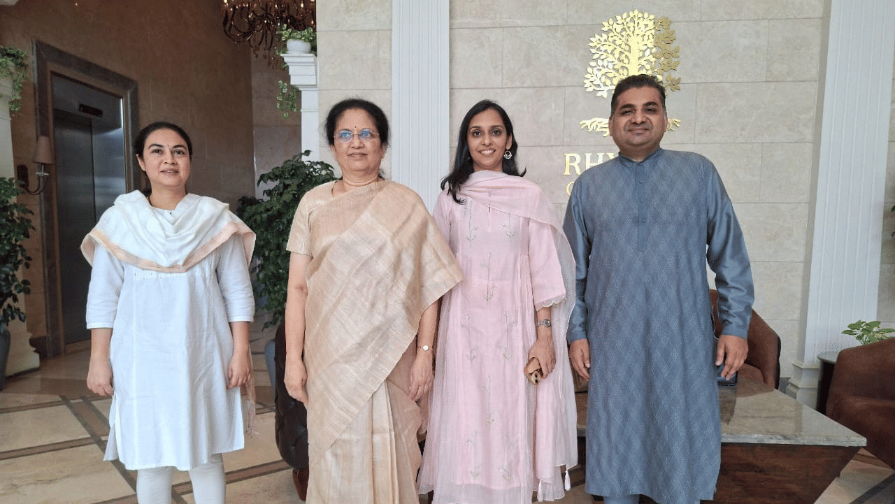 Group photo of four people in traditional attire standing in the lobby of Rhythm Hospitality hotel, with the hotel logo in the background.